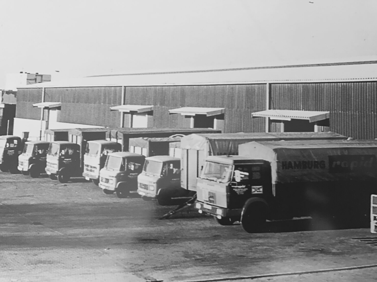 Reihe von Rapid-Lkw an der Laderampe einer Lagerhalle, 1960er Jahre